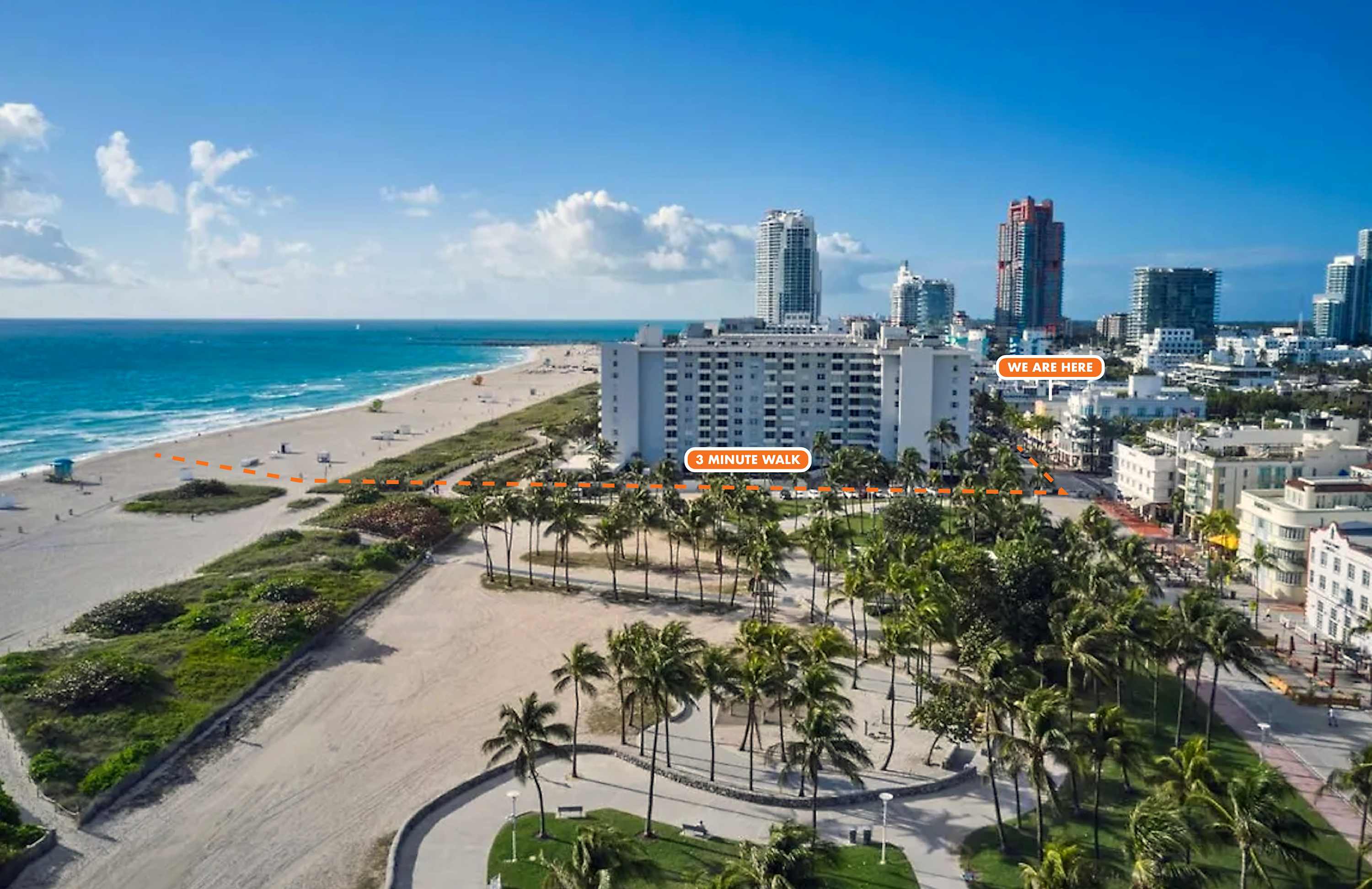 An aerial view of a beachfront property with palm trees and city skyline in the background.
